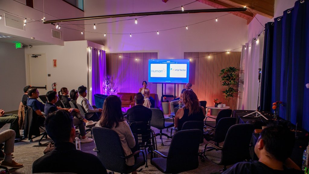 The room during a Founder's Plateau evening: string lights overhead, founders seated facing the two chairs up front
